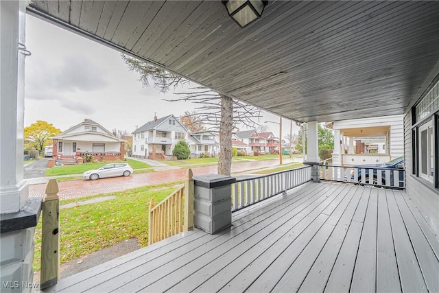 wooden deck featuring a residential view, a lawn, and a porch