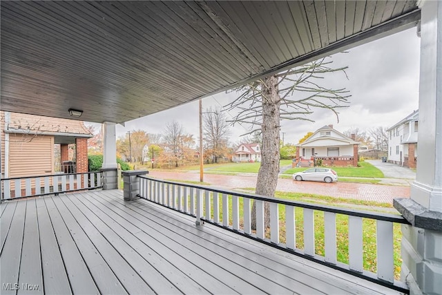 wooden terrace featuring a residential view, a lawn, and covered porch