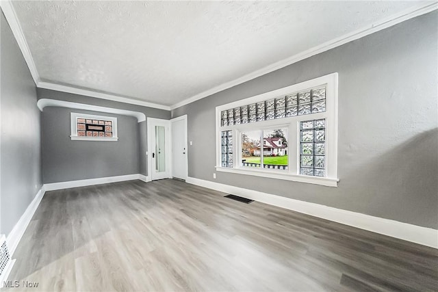 empty room with visible vents, crown molding, and baseboards