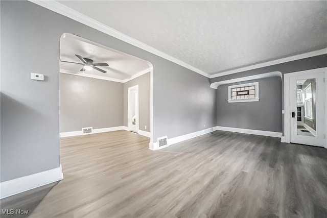 unfurnished living room with wood finished floors, baseboards, visible vents, and ornamental molding