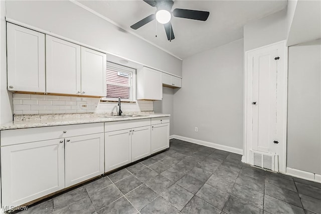 kitchen featuring visible vents, a sink, vaulted ceiling, white cabinets, and backsplash