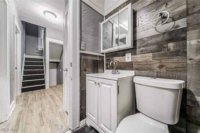 bathroom with toilet, wood finished floors, vanity, and wood walls