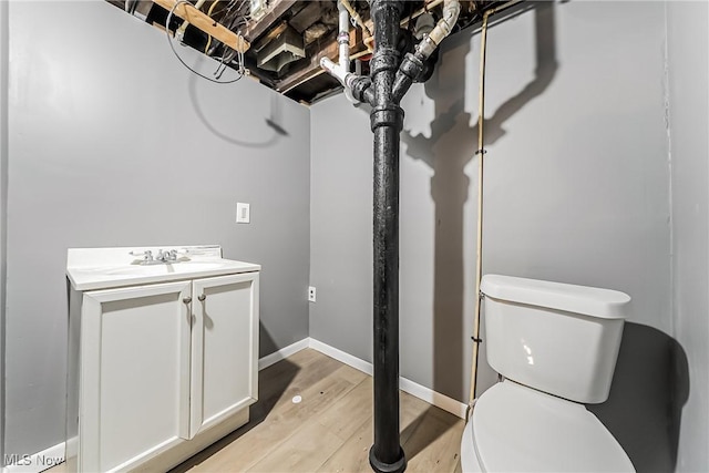 half bathroom featuring vanity, toilet, wood finished floors, and baseboards