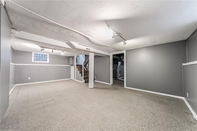 below grade area featuring stairway, baseboards, a textured ceiling, and rail lighting