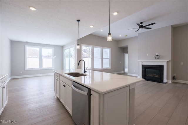 kitchen with a sink, stainless steel dishwasher, open floor plan, light wood-style flooring, and a glass covered fireplace