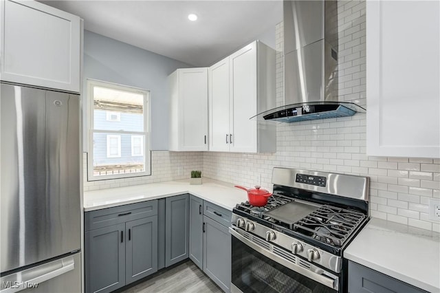 kitchen featuring gray cabinetry, wall chimney range hood, backsplash, stainless steel appliances, and light countertops