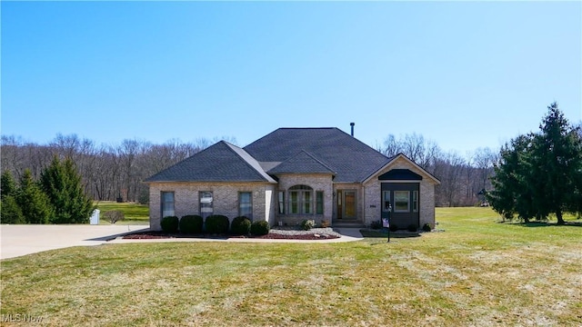 french country style house featuring a front lawn, a view of trees, and brick siding