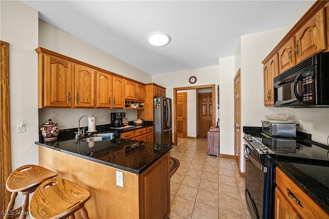 kitchen featuring brown cabinetry, a sink, electric stove, black microwave, and stainless steel fridge