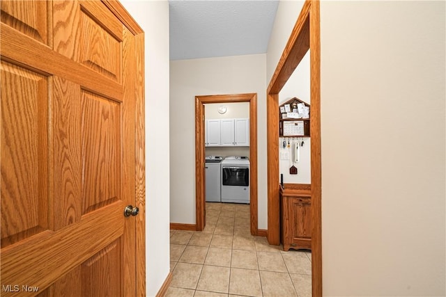 corridor featuring light tile patterned flooring, separate washer and dryer, baseboards, and a textured ceiling