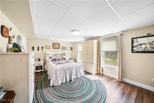 bedroom with a drop ceiling, light wood-type flooring, and baseboards