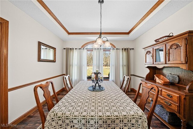 dining space featuring baseboards, a raised ceiling, and ornamental molding