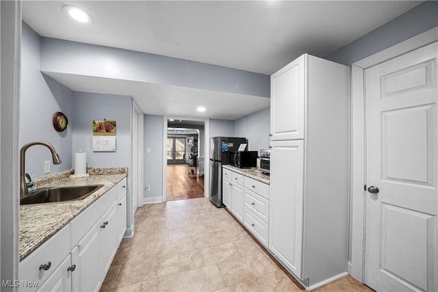 kitchen featuring light stone counters, recessed lighting, freestanding refrigerator, a sink, and white cabinets