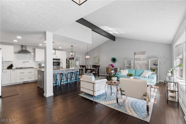 living area featuring dark wood-type flooring, vaulted ceiling with beams, a healthy amount of sunlight, and a textured ceiling