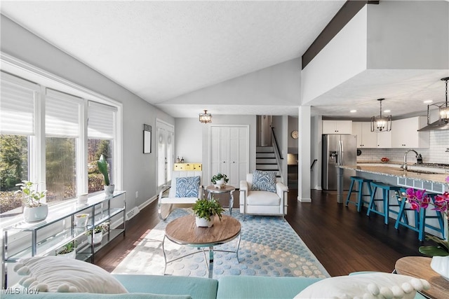 living room with lofted ceiling, dark wood finished floors, baseboards, a chandelier, and stairs