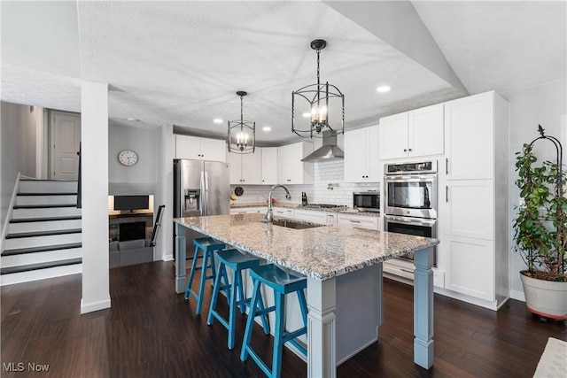 kitchen with a sink, backsplash, wall chimney range hood, stainless steel appliances, and dark wood-style flooring