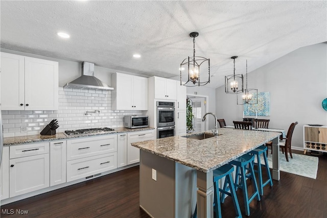 kitchen with dark wood-style floors, appliances with stainless steel finishes, wall chimney exhaust hood, and a sink