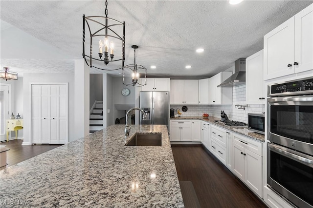 kitchen featuring dark wood-type flooring, a sink, backsplash, appliances with stainless steel finishes, and wall chimney range hood