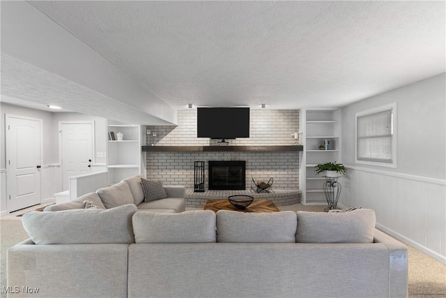 carpeted living room with wainscoting, built in shelves, a textured ceiling, and a brick fireplace