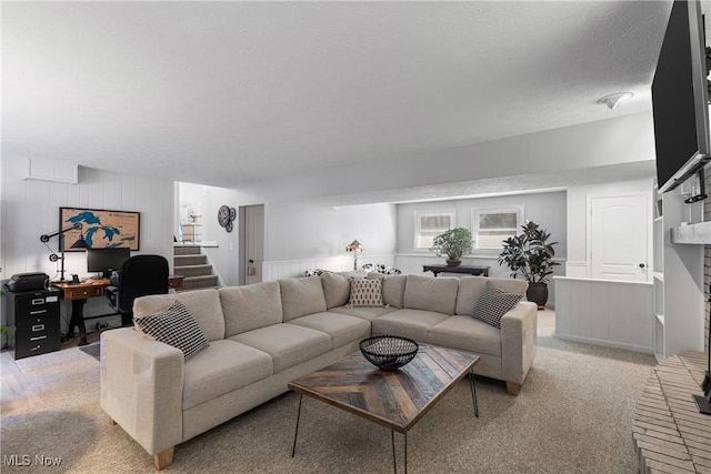 living area with light carpet, a textured ceiling, and stairs