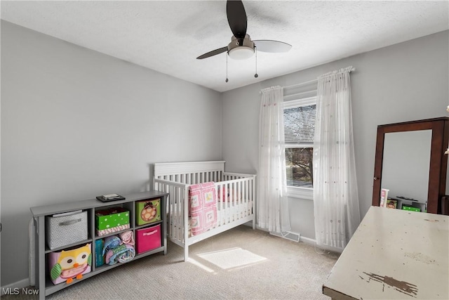 carpeted bedroom featuring visible vents, ceiling fan, baseboards, a textured ceiling, and a nursery area