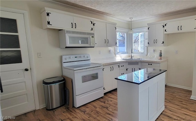 kitchen with a sink, a textured ceiling, wood finished floors, white cabinetry, and white appliances