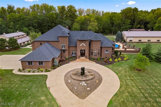 view of front of home featuring brick siding, curved driveway, a shingled roof, a front yard, and a chimney