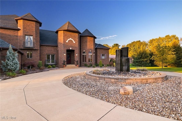 view of front of home with brick siding, curved driveway, and a shingled roof