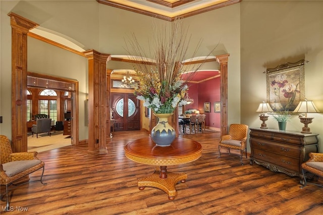 entryway featuring a notable chandelier, wood finished floors, a high ceiling, crown molding, and decorative columns