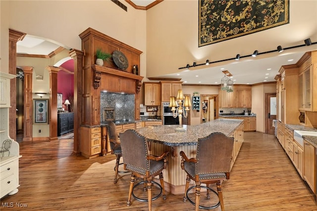 kitchen with visible vents, a kitchen bar, a spacious island, arched walkways, and light wood-style floors