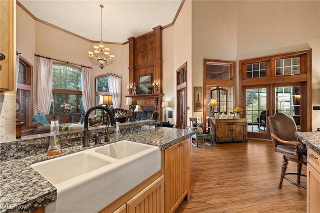 kitchen with a notable chandelier, light wood-style flooring, a sink, a large fireplace, and crown molding