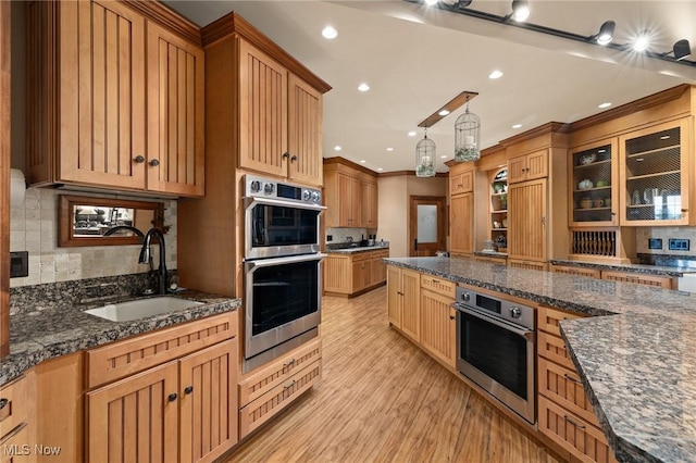 kitchen featuring dark stone countertops, light wood-type flooring, a sink, double oven, and tasteful backsplash