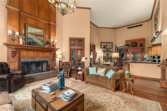 living room featuring wood finished floors, an inviting chandelier, ornamental molding, a towering ceiling, and a brick fireplace