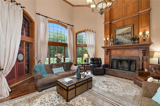 living room featuring a notable chandelier, ornamental molding, wood finished floors, a high ceiling, and a fireplace