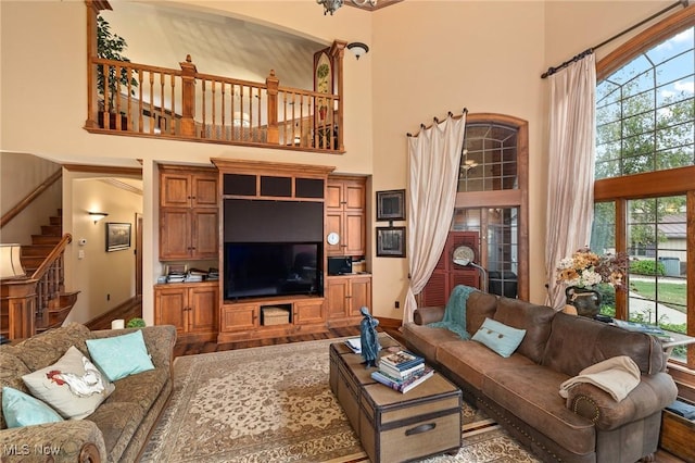 living area featuring a wealth of natural light, stairway, wood finished floors, and a towering ceiling