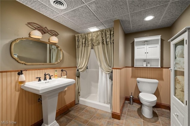 bathroom with visible vents, a shower stall, a drop ceiling, a wainscoted wall, and toilet