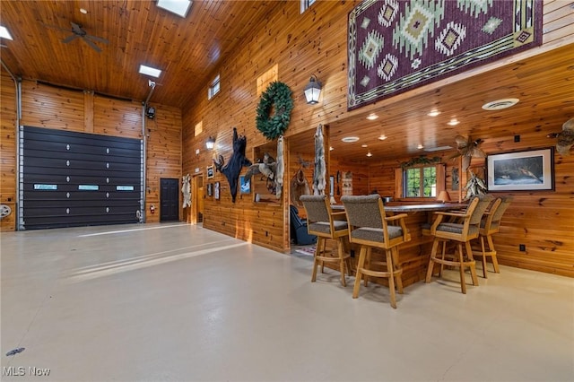 dining room featuring wooden walls, wood ceiling, concrete flooring, and a ceiling fan