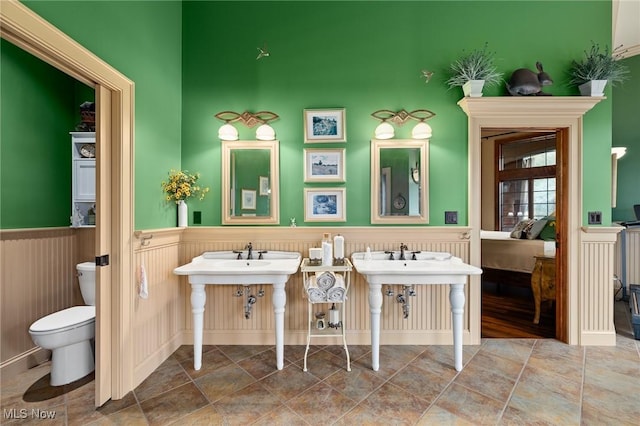 bathroom with ensuite bath, toilet, and a wainscoted wall