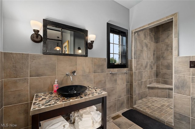 full bath with a sink, tiled shower, tile walls, and wainscoting