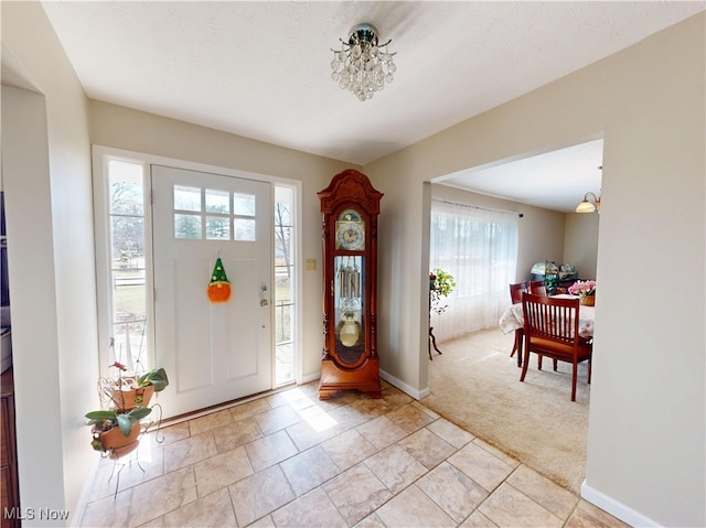 entrance foyer featuring a notable chandelier, light colored carpet, baseboards, and a textured ceiling