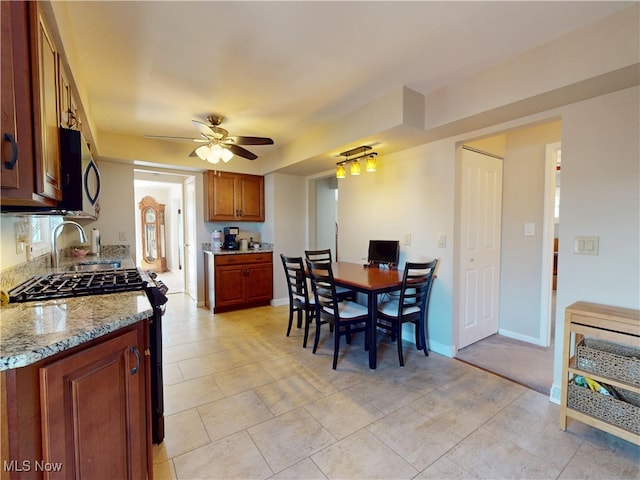 kitchen with stainless steel appliances, a ceiling fan, baseboards, and light stone countertops