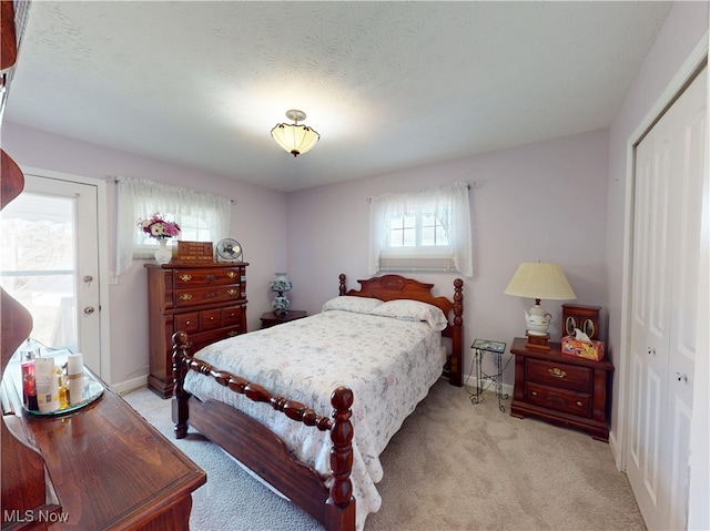 bedroom featuring a closet, light colored carpet, a textured ceiling, and baseboards