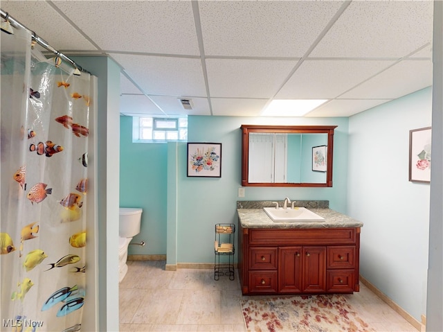 bathroom featuring vanity, a shower with shower curtain, baseboards, a drop ceiling, and toilet