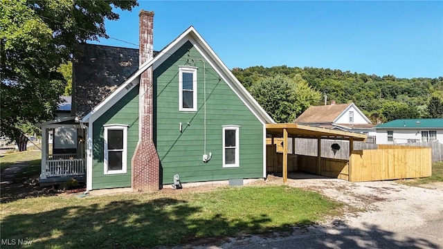 exterior space with a lawn, dirt driveway, fence, an attached carport, and a chimney