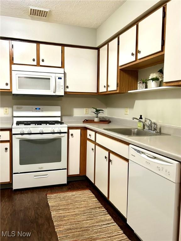 kitchen featuring white appliances, a textured ceiling, light countertops, and a sink