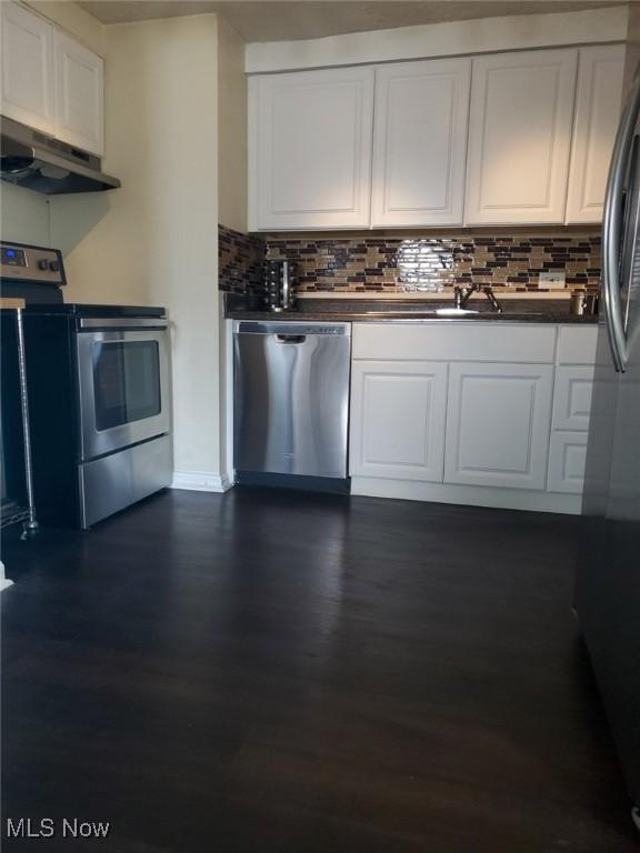 kitchen with under cabinet range hood, white cabinets, appliances with stainless steel finishes, and dark wood-style flooring