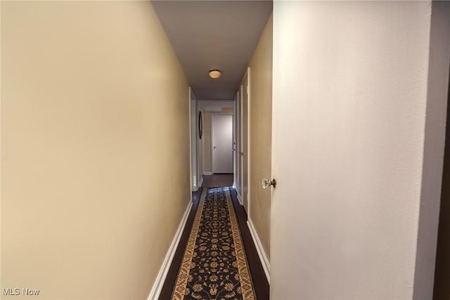 hallway featuring dark carpet and baseboards