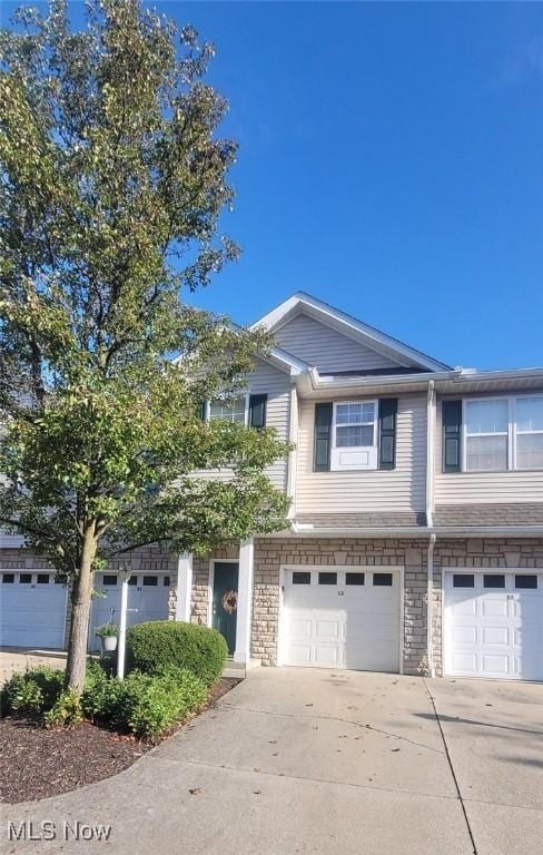 multi unit property featuring stone siding, an attached garage, and driveway