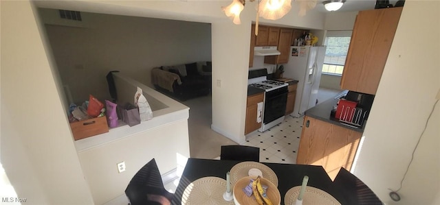 kitchen featuring visible vents, under cabinet range hood, range with gas stovetop, white fridge with ice dispenser, and light floors