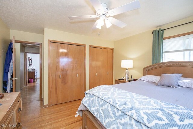 bedroom with two closets, a ceiling fan, light wood finished floors, and a textured ceiling