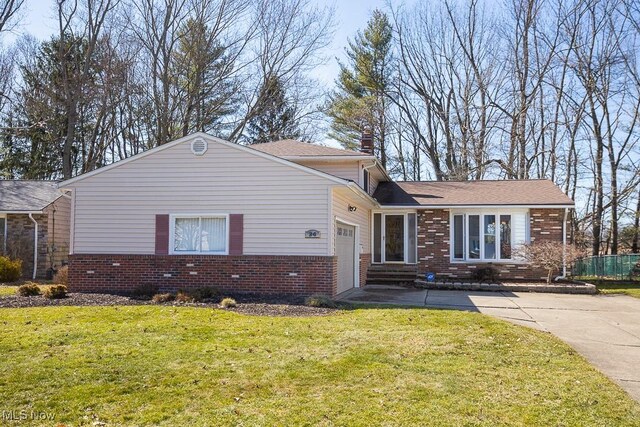 split level home featuring a front yard, an attached garage, brick siding, and driveway